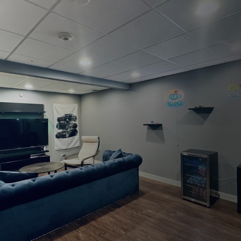 Cozy basement living room with blue couch, TV, gray walls, and wall shelves