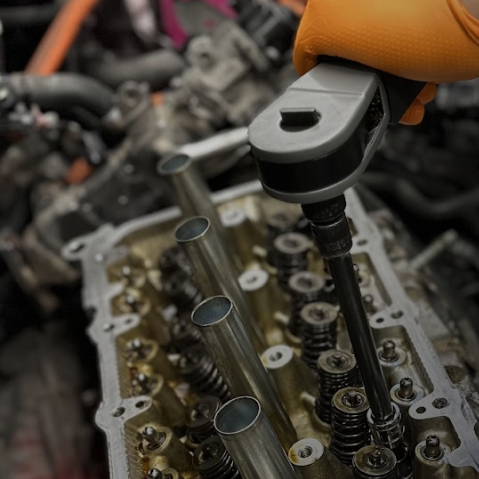 Gloved hand using a wrench on an engine cylinder head during repair