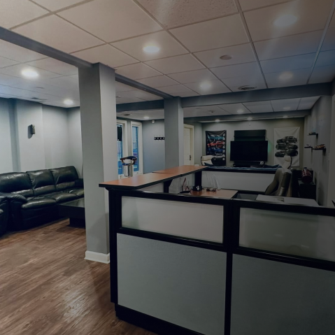 Empty office reception area with black-and-white desk, gray columns, and leather couches under fluorescent lights