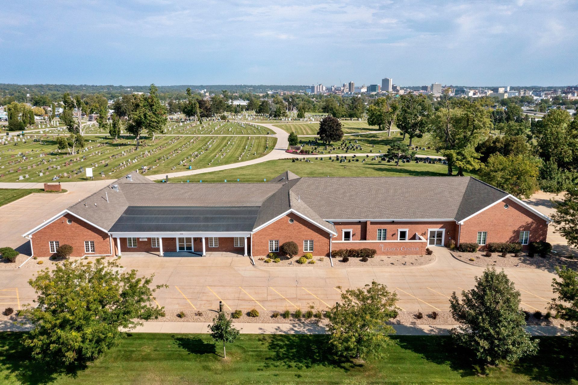 Aerial view of a red-brick building with a gray roof, surrounded by trees and open grounds.