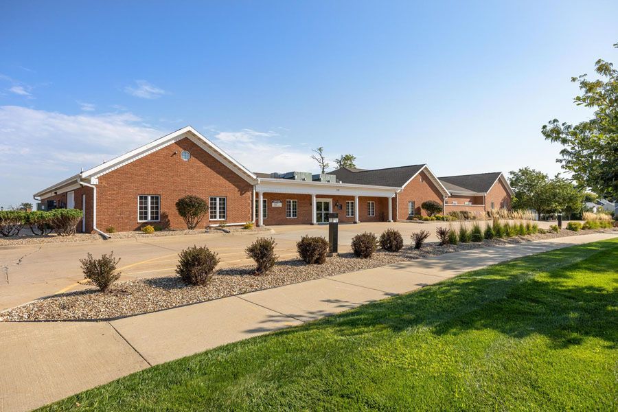 Brick apartment complex with tan roofs, desert landscaping, and a green lawn under a clear blue sky