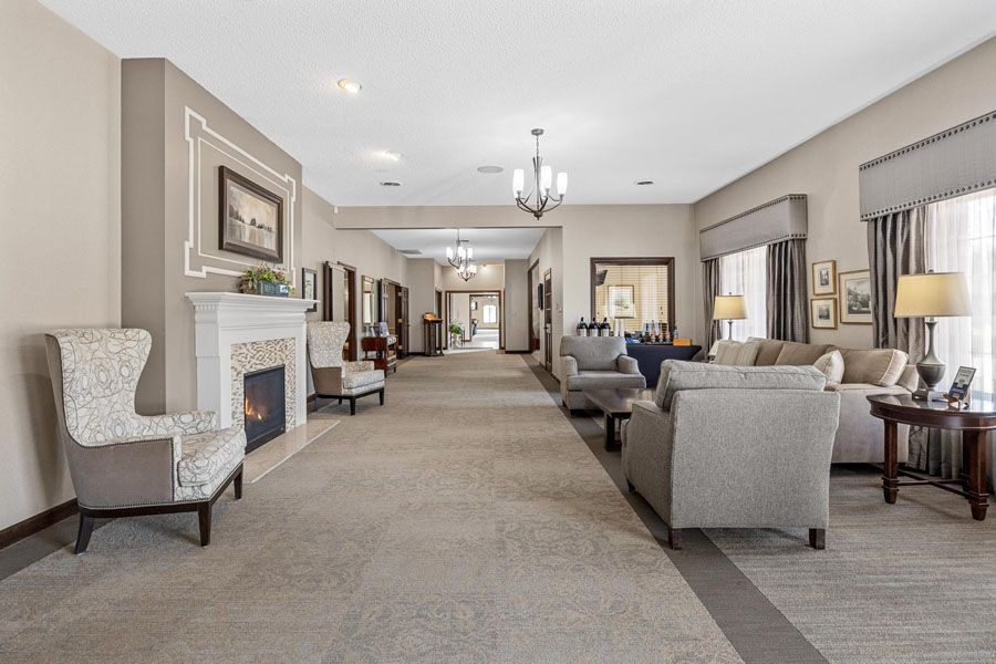 Spacious beige lounge with fireplace, armchairs, sofas, and chandelier in a bright hallway