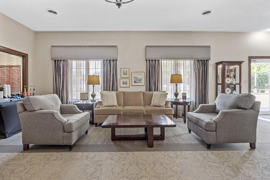 Spacious living room with beige and gray sofas, coffee table, lamps, and large windows with curtains