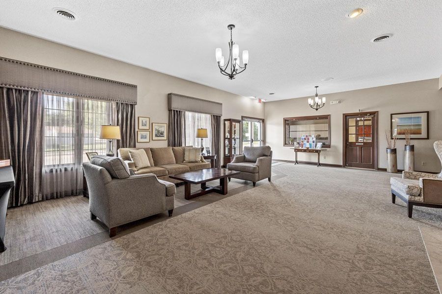Spacious beige living room with carpet, sofas, armchairs, chandeliers, and large windows