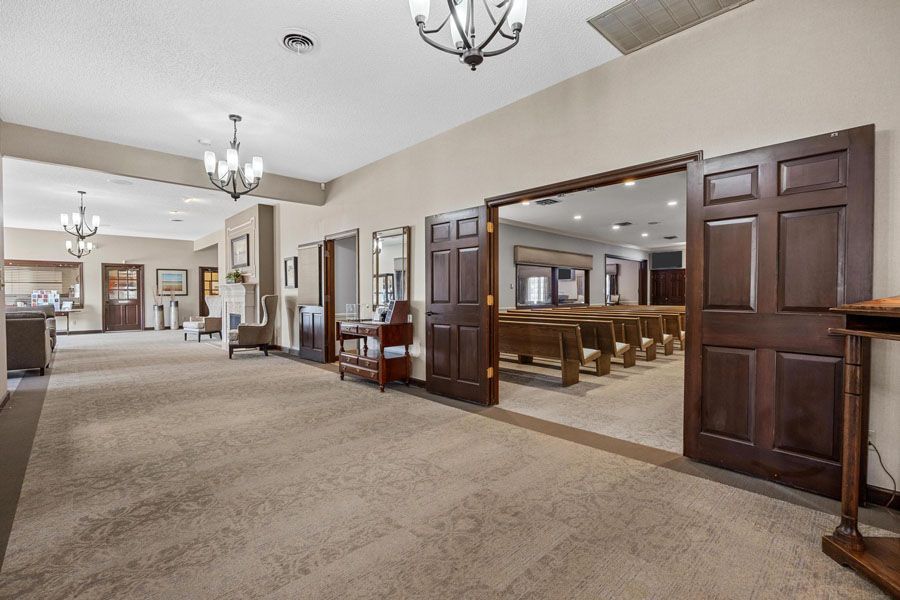 Wide carpeted hall with wood-paneled double doors, chandeliers, and a large meeting room visible through open doors.