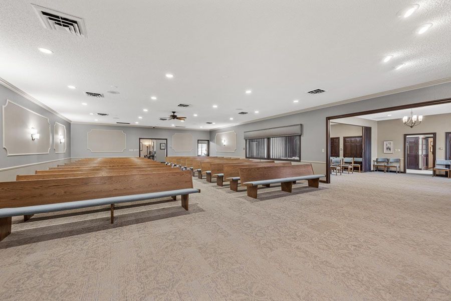 Spacious empty banquet hall with rows of wooden benches and beige carpet under bright ceiling lights