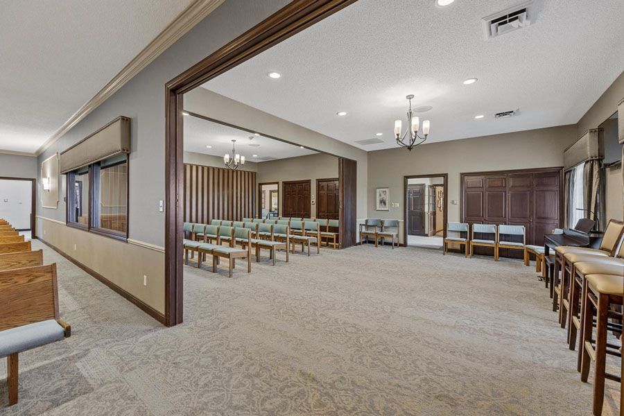 Spacious carpeted hall with rows of chairs, wood trim, and chandeliers in a community room