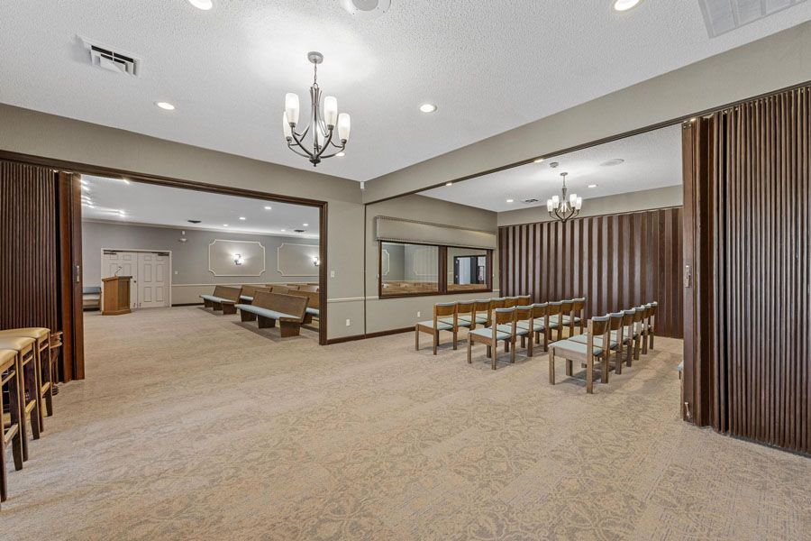 Spacious beige banquet hall with rows of chairs, tables, and chandeliers under recessed lighting