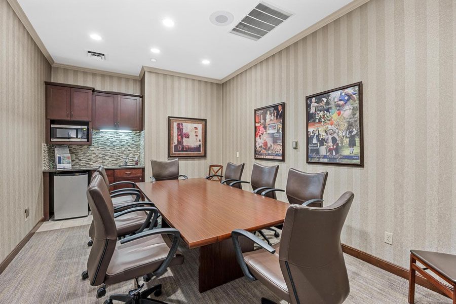 Conference room with wooden table, black chairs, wall art, and kitchenette area