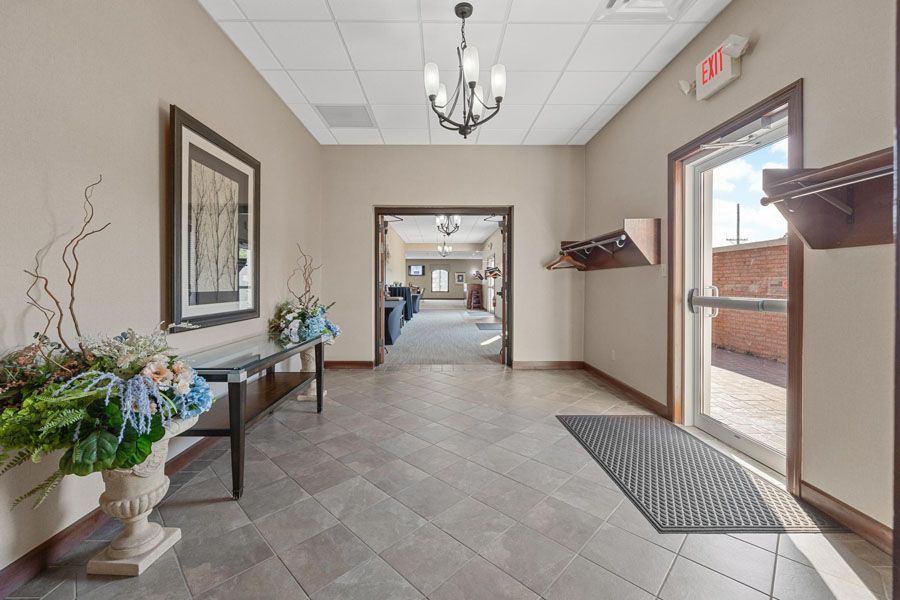 Bright lobby hallway with tiled floor, floral arrangement, wall art, and glass exit doors.