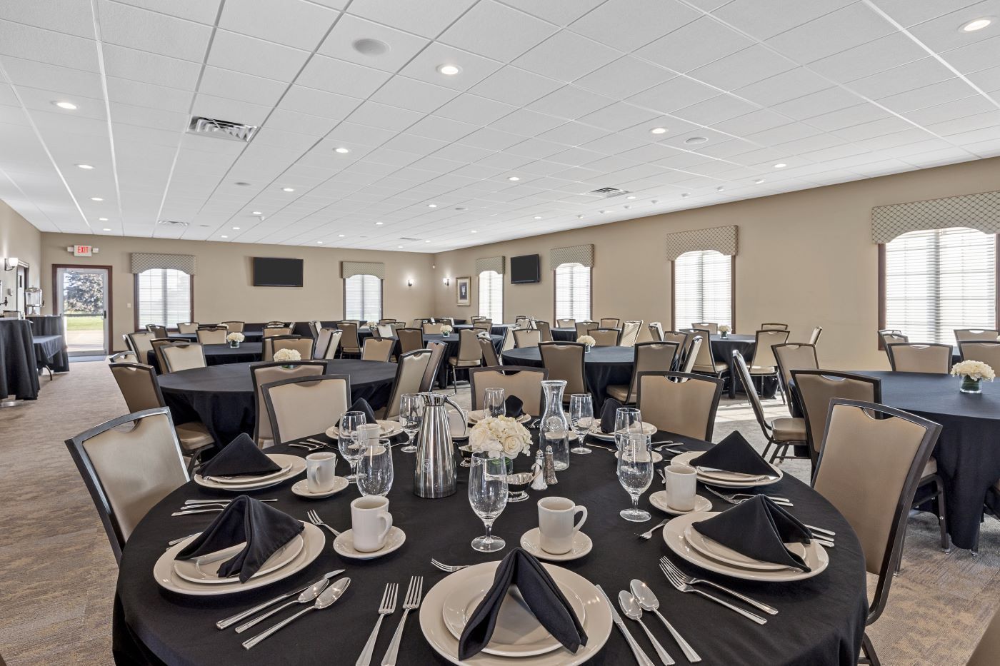Banquet hall with round tables set for an event, black tablecloths, and beige chairs