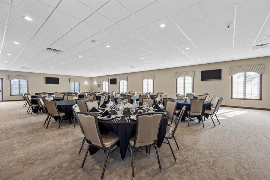 Spacious banquet hall with round tables, black chair covers, and beige carpet under bright ceiling lights