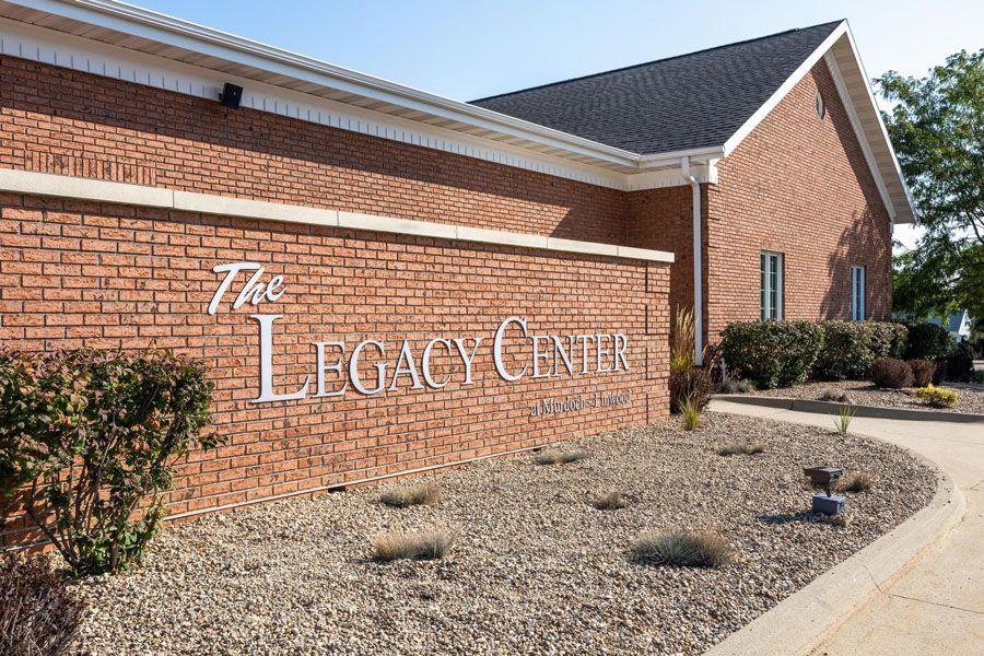 Brick building exterior with “The Legacy Center” sign and landscaped gravel front path