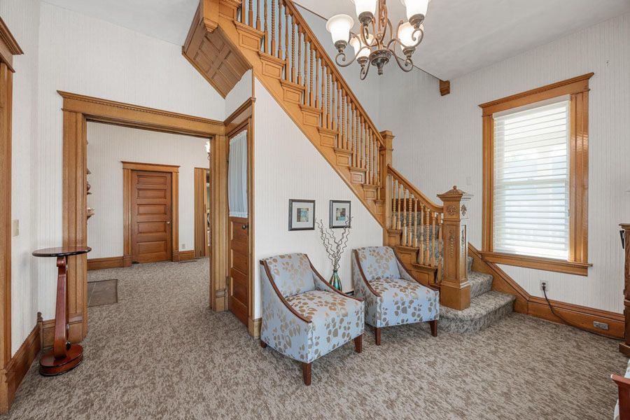 Entry hall with staircase, chandelier, and two patterned chairs in a carpeted room