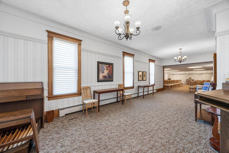 Spacious empty room with carpet, windows, chandeliers, and a piano along the left wall.