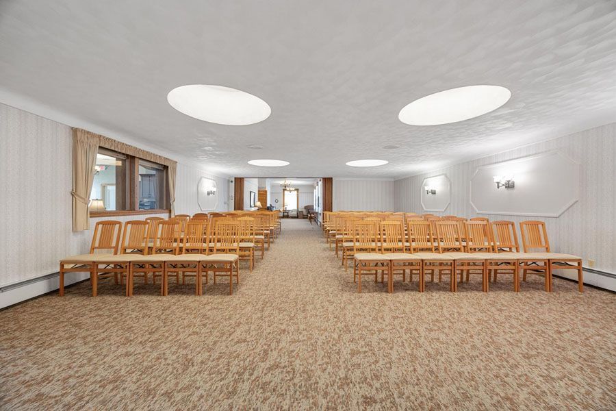 Spacious white meeting room with rows of wooden chairs and carpeted floor, lit by round ceiling lights