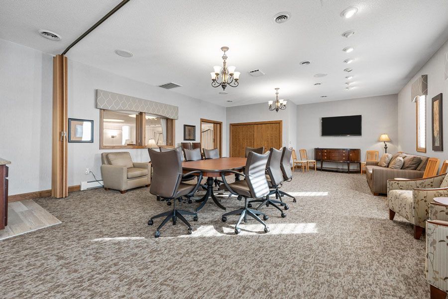Spacious community lounge with carpet, chairs, tables, chandelier, and wall-mounted TV