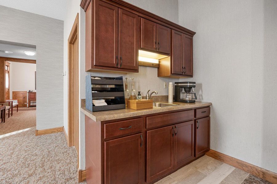 Kitchenette with wood cabinets, sink, microwave, and coffee maker in a bright hallway alcove