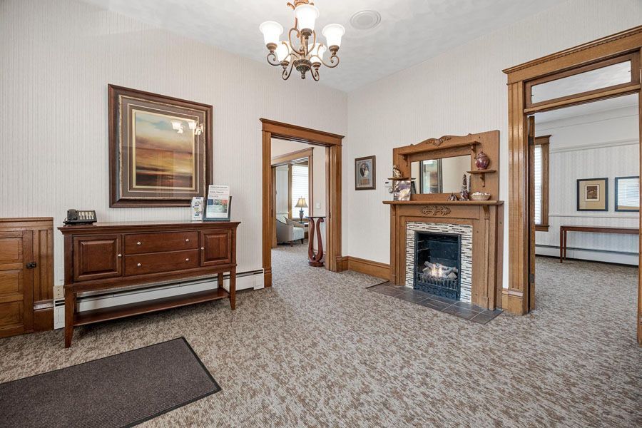 Spacious living room with carpet, wooden furniture, fireplace, mirror, and adjoining doorway.