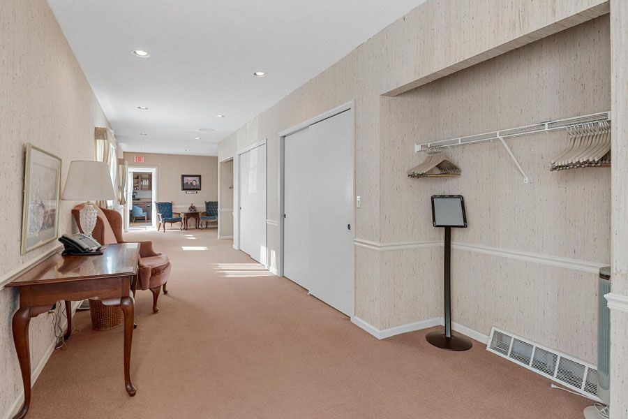 Bright hallway with beige carpet, white walls, a wood desk, and a coat rack by closet doors.