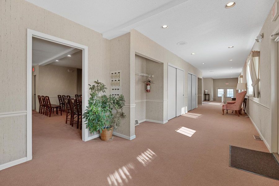 Bright hallway with beige carpet, white walls, potted plant, and seating room visible through open doorway