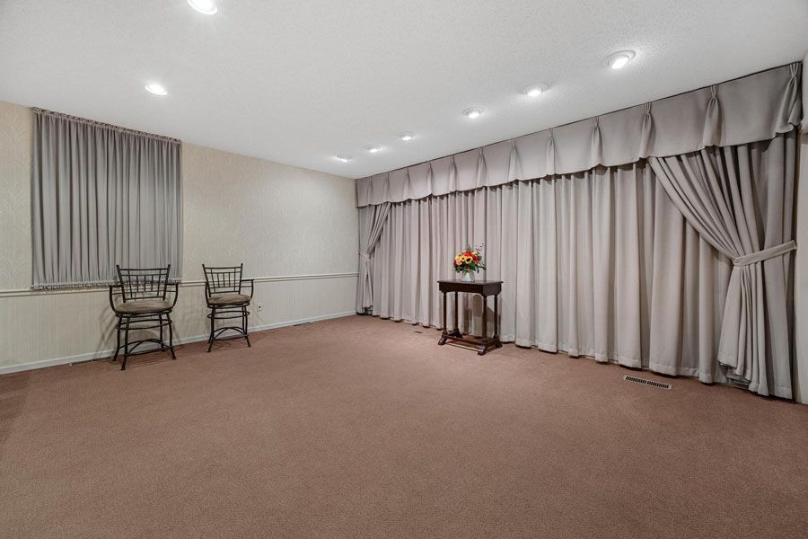 Empty carpeted room with beige curtains, two chairs by a window, and a small table near the wall