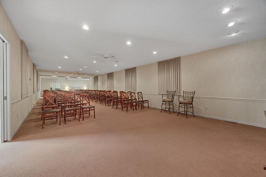 Large empty banquet hall with rows of stacked chairs and beige carpet under recessed ceiling lights