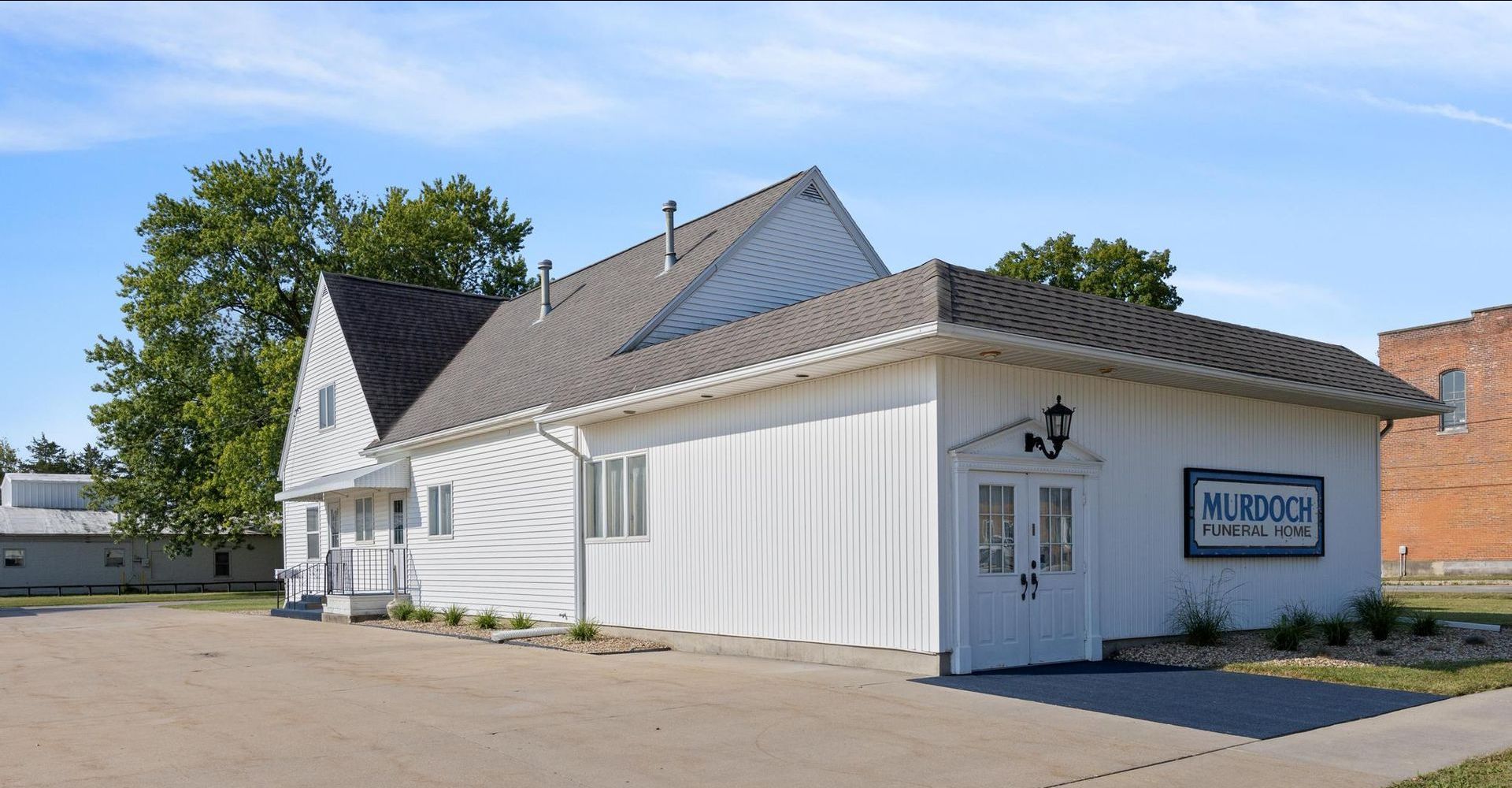 White building with a sign, gray roof, and parked car on a sunny day