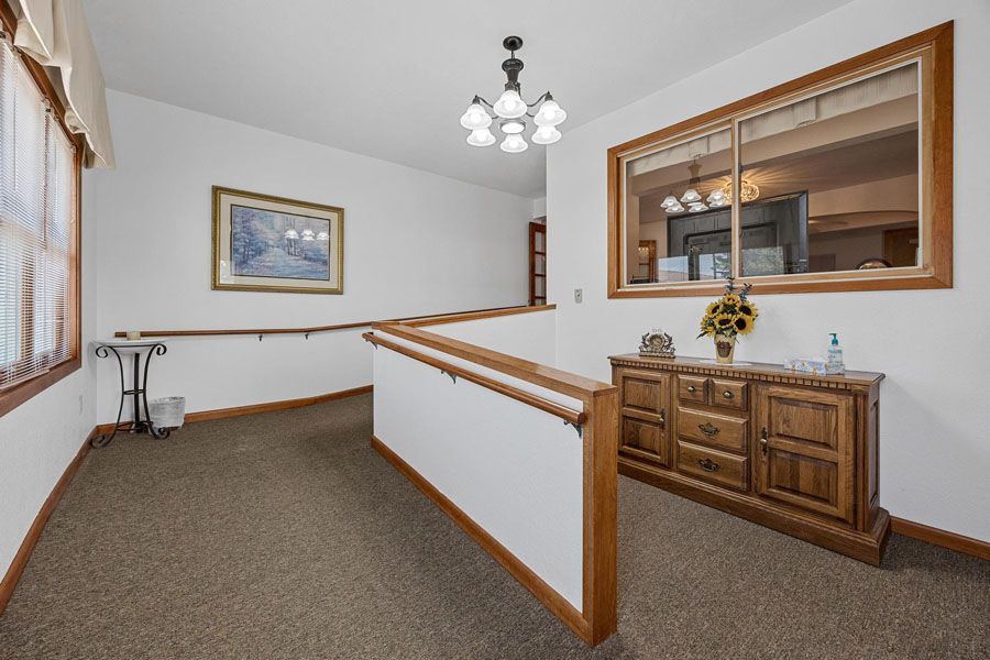 Hallway with carpeted floor, white walls, wooden trim, framed art, and a sideboard beneath a pass-through window.