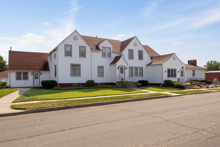 Large white suburban house with red roof accents and a manicured lawn beside a quiet street