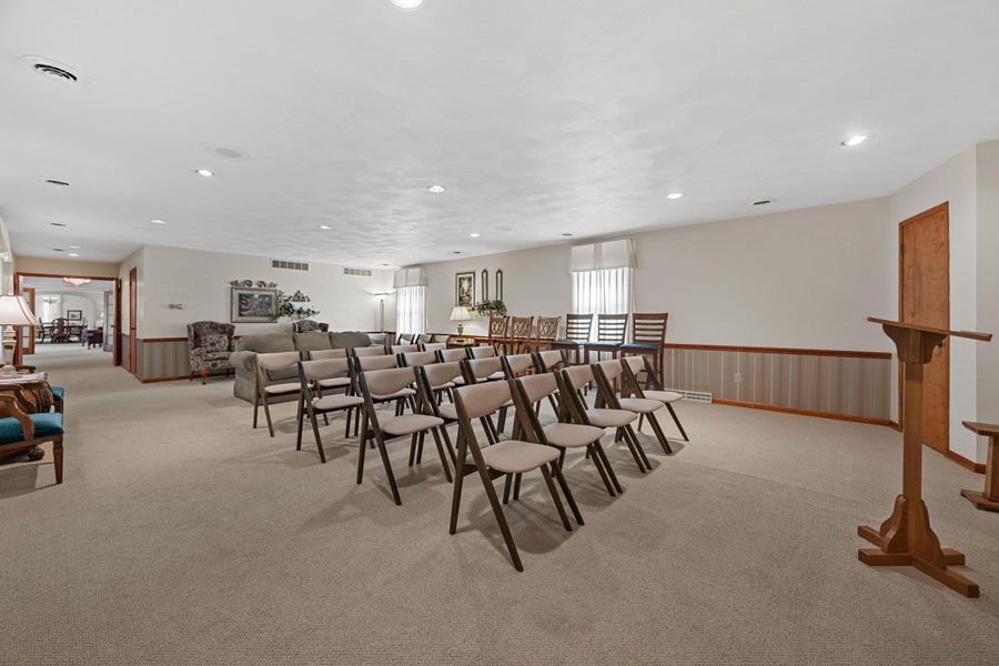 Empty church hall with rows of folding chairs, beige carpet, white walls, and a wooden lectern.