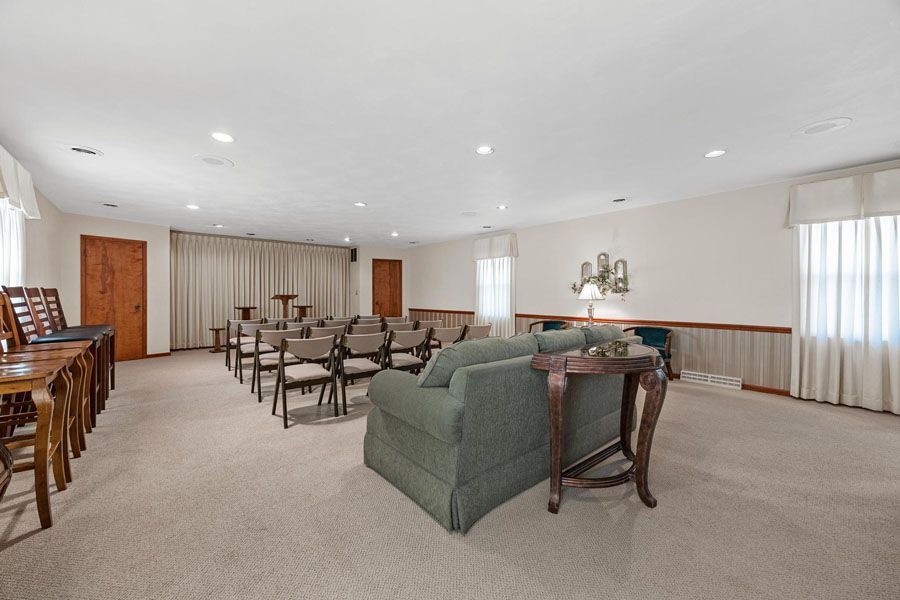 Spacious carpeted living room with green sofa, dining tables, and curtained windows.