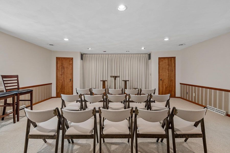 Empty small auditorium with rows of beige chairs, wood paneling, and stage seating at the front