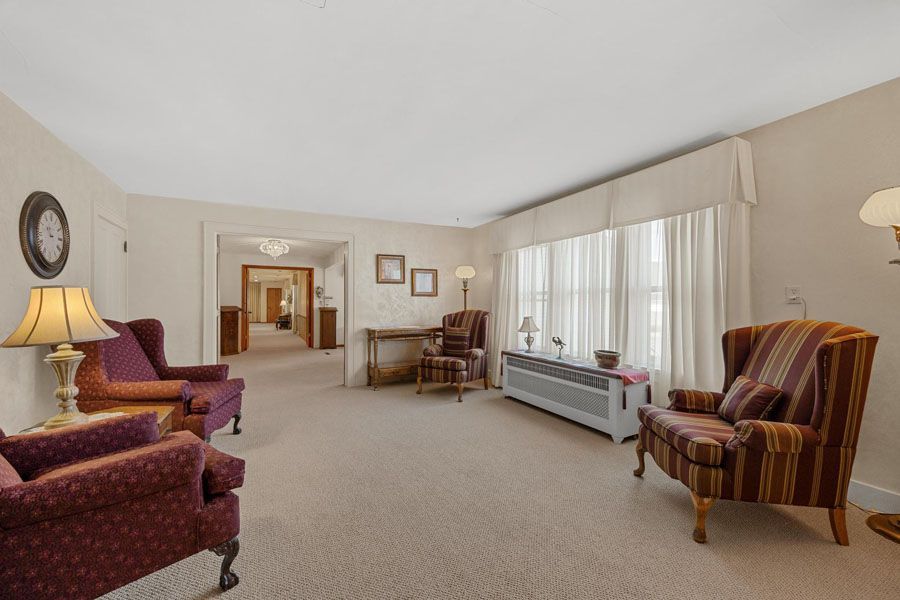 Spacious beige living room with burgundy armchairs, striped chair, and large window with sheer curtains