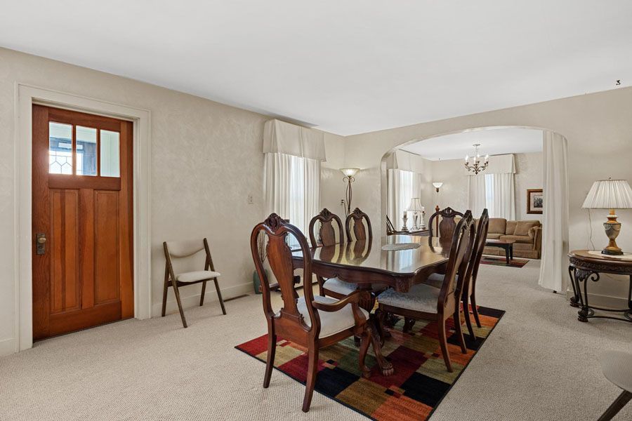 Dining room with wooden table and chairs, mirrored wall, and beige carpet beside a wooden door.