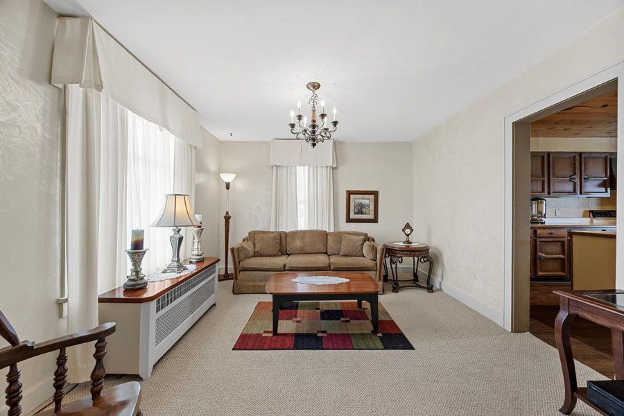 Bright living room with beige sofa, patterned rug, chandelier, and open view to kitchen and dining area