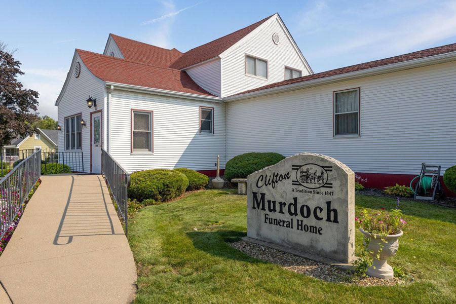 Murdoch Funeral Home building with a sign, white siding, red roof, and a walkway