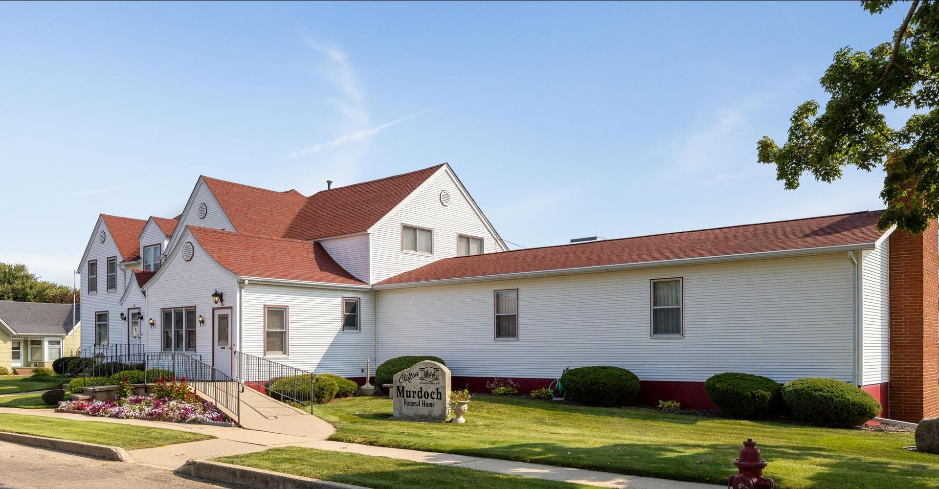 Large white house with red roof and landscaped yard on a sunny day