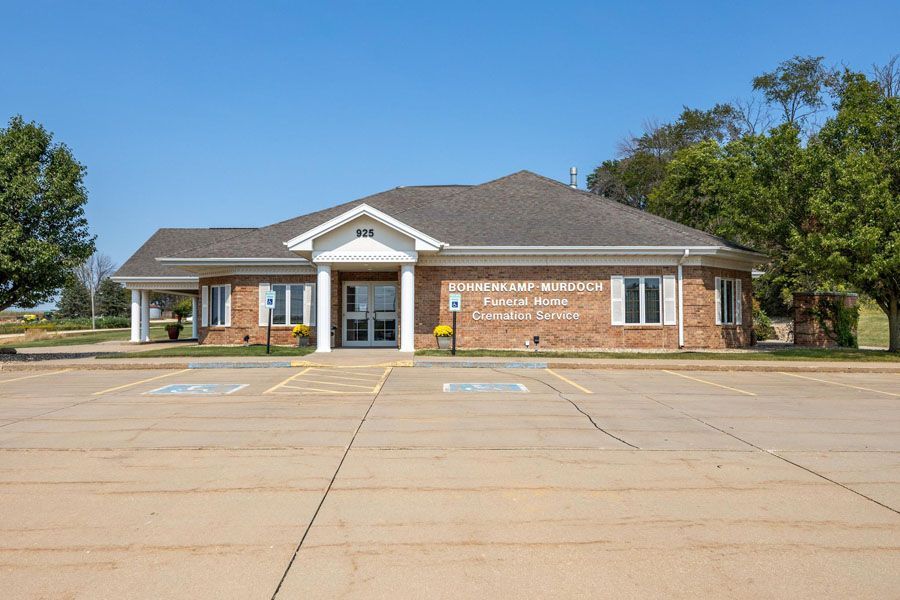Single-story brick building with white columns and a large empty parking lot on a sunny day