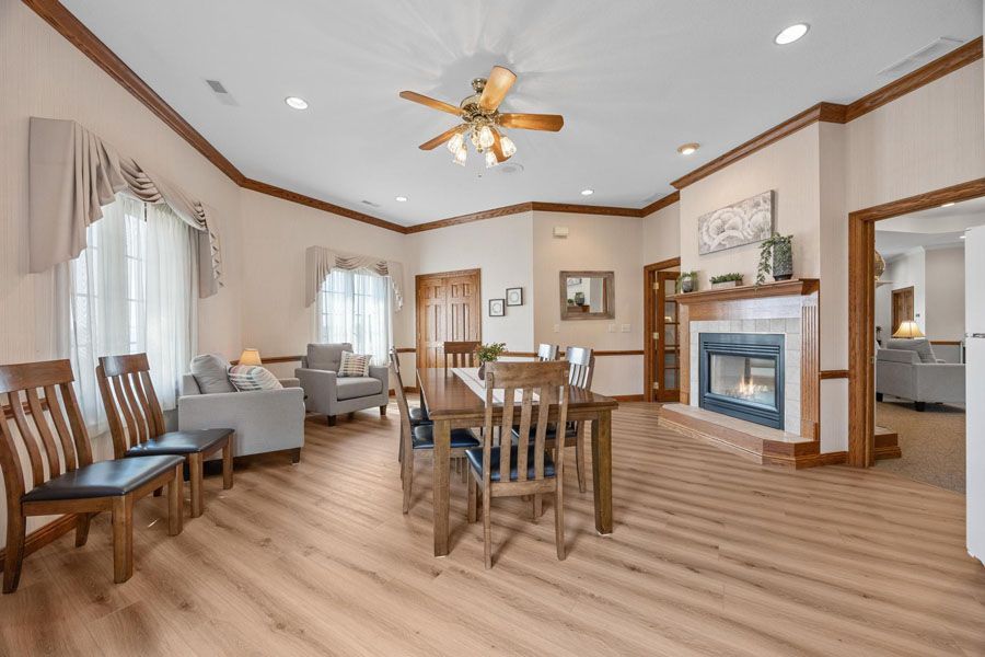 Spacious living-dining room with wood flooring, fireplace, gray sofa, and dining table under a ceiling fan