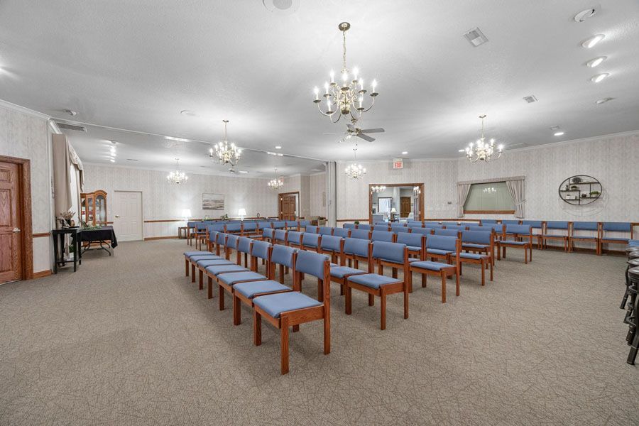 Empty church sanctuary with rows of wooden benches, carpeted floor, and chandeliers under a white ceiling
