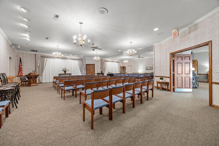 Empty chapel interior with rows of wooden benches, chandeliers, and an altar at the front