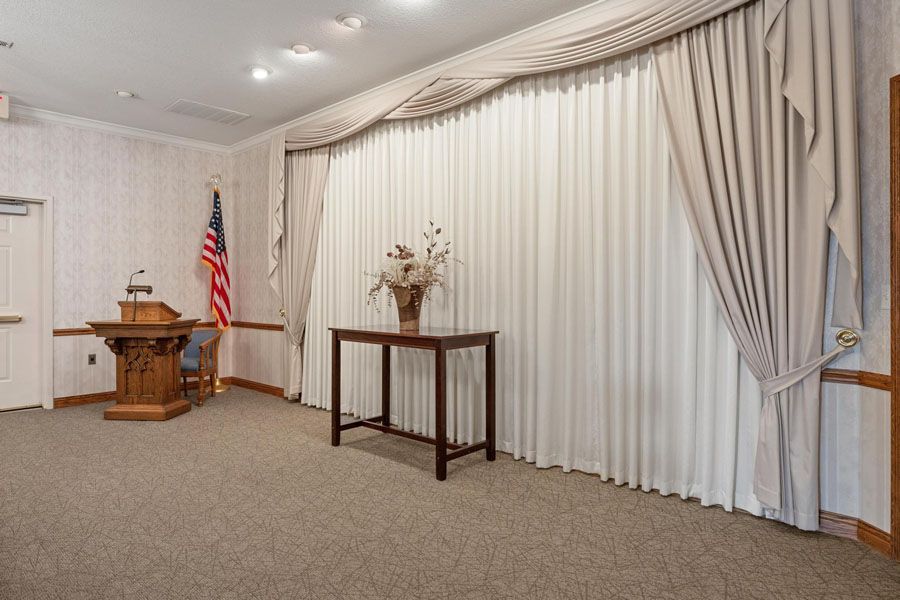 Small chapel or meeting room with pulpit, American flag, table, and draped white curtains