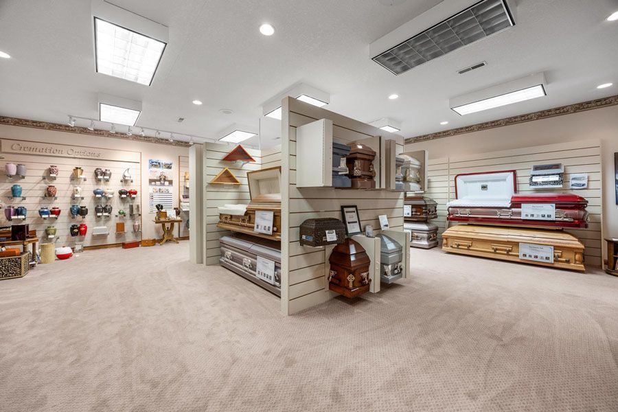 Spacious showroom with beige carpet, shelves of decor, baskets, wall art, and stacked rugs under bright ceiling lights