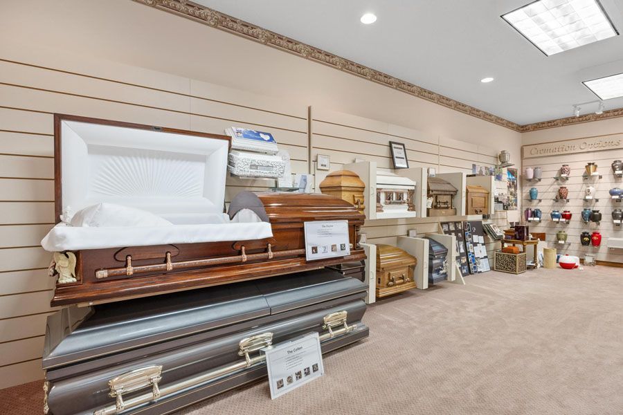 Casket showroom with an open white casket on a wooden display and funeral urns along the wall