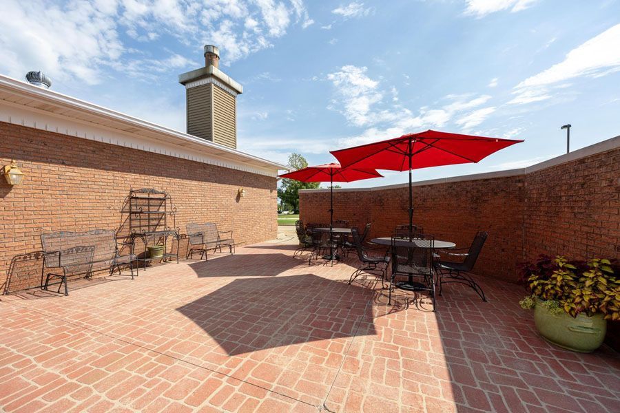 Brick patio with outdoor tables, chairs, and red umbrellas beside brick walls under a blue sky