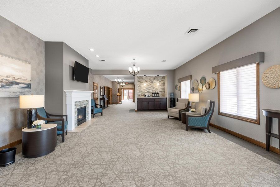 Modern lobby with gray carpet, fireplace, seating area, and large windows with blinds