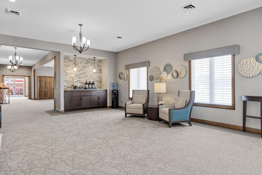 Bright lounge with beige carpet, fireplace, armchairs, windows, and chandelier.
