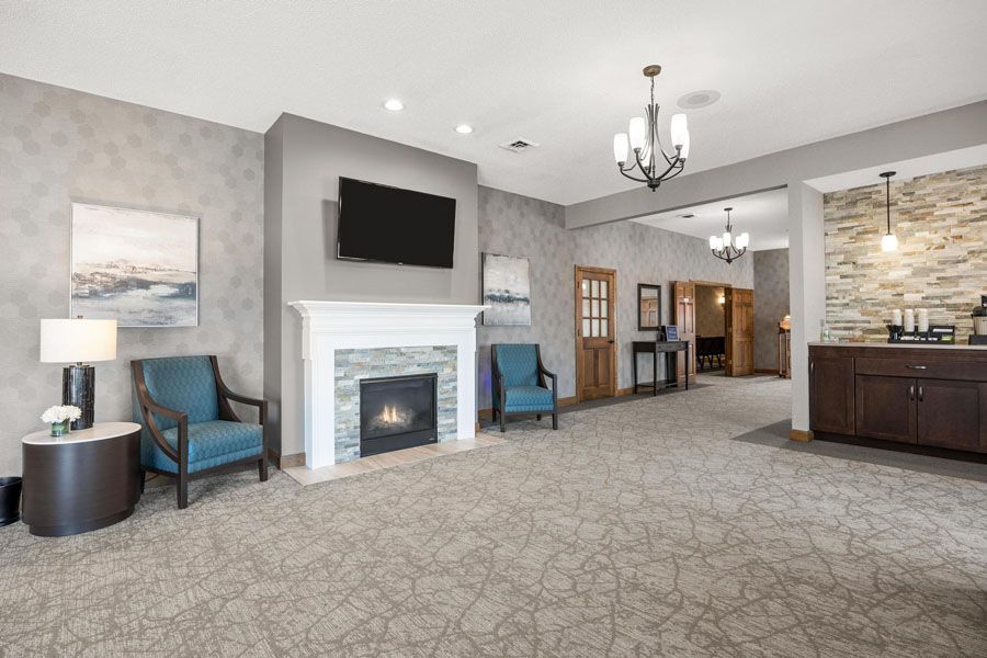 Spacious living room with fireplace, TV, blue chairs, chandelier, and open dining area