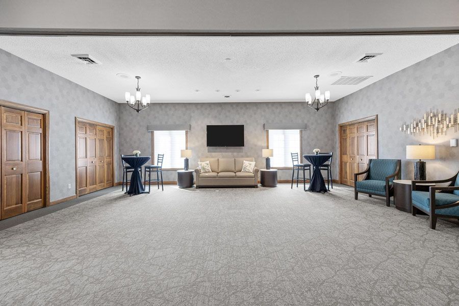 Spacious beige event hall with carpet, sofas, cocktail tables, wall-mounted TV, and doors on both sides